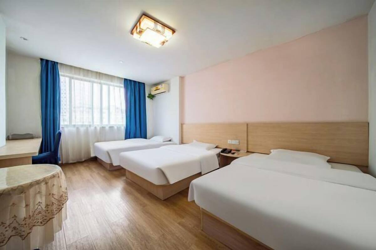 Habitació d'hotel amb tres llits, una taula de nit, un escriptori i una finestra amb cortines.