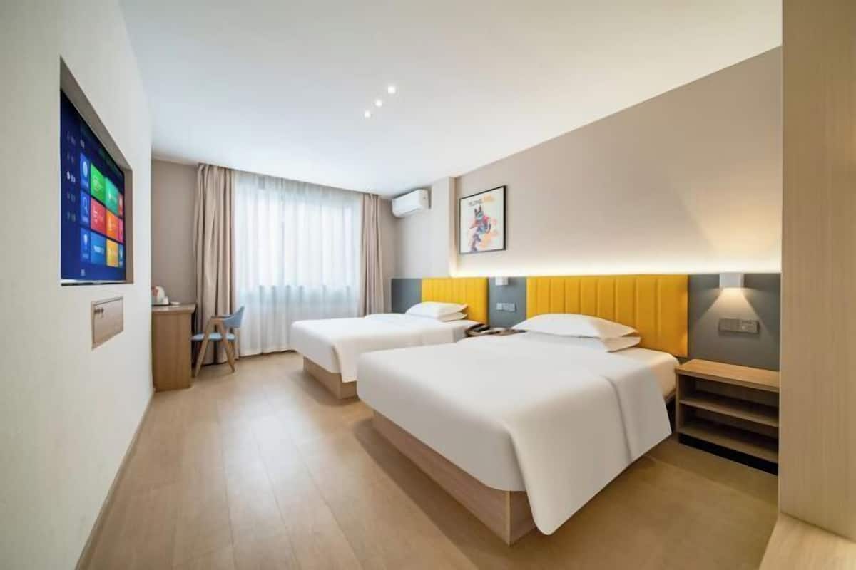 Habitació d'hotel amb dos llits, una escriptori, una cadira, un televisor i una finestra amb cortines.