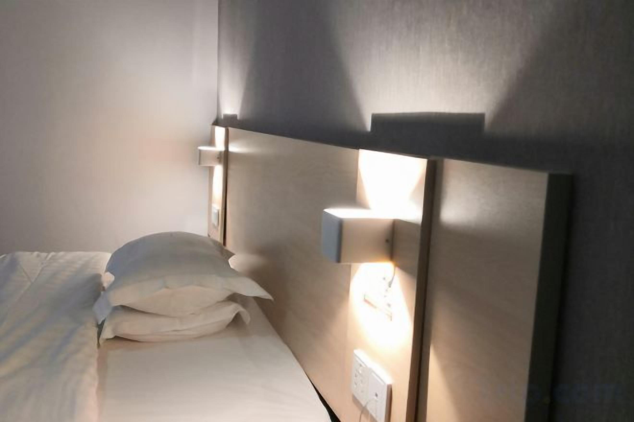 Un lit avec une literie et des oreillers blancs, une table de chevet et un luminaire fixé au mur.