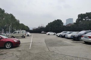 Un estacionamiento con varios autos y una camioneta, rodeado de árboles y edificios.