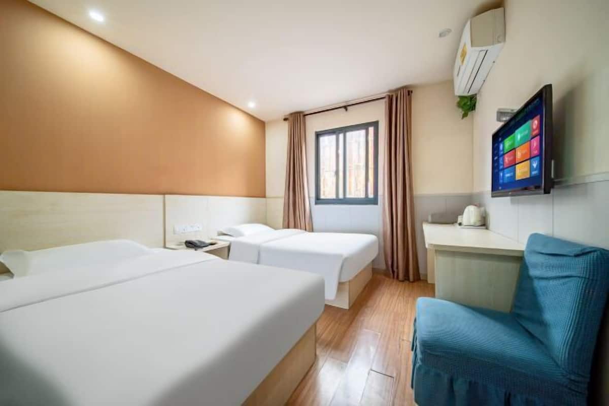 Habitació d'hotel amb dos llits, una taula de treball, una cadira, un televisor i una finestra amb cortines.