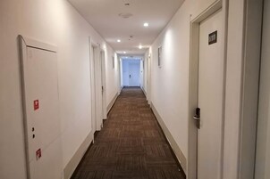 Un pasillo de hotel con puertas a ambos lados, suelo alfombrado y pared de color claro.
