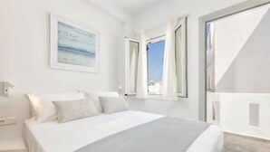 Un dormitori amb un llit, una finestra amb cortines, una làmpada penjada a la paret i una fotografia amb marc.