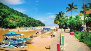 Una zona junto al río con barcos amarrados, una playa de arena y abundante vegetación.