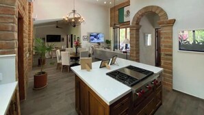 Una cocina amplia con una isla central, comedor y sala de estar con televisor.
