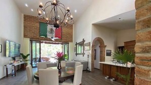 Un amplio salón con una mesa de comedor, asientos cómodos, una araña y vistas al exterior.