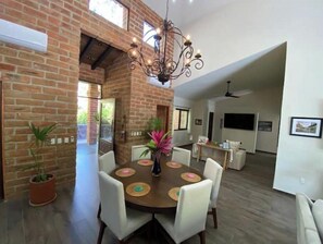A dining area with a brick wall, a chandelier, and a round table with white chairs.