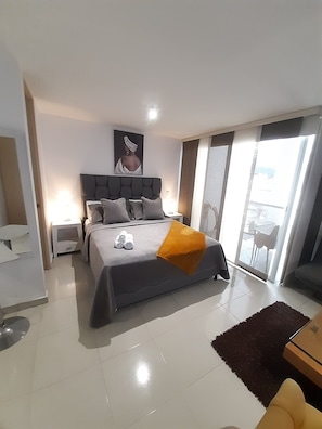 Ein modernes Schlafzimmer mit einem großen Bett, einem Nachttisch, einer Schublade und Blick nach draußen durch eine Schiebetür.