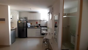 Een compacte keuken met witte kastjes, een koelkast, een spoelbak en een kleine eethoek.