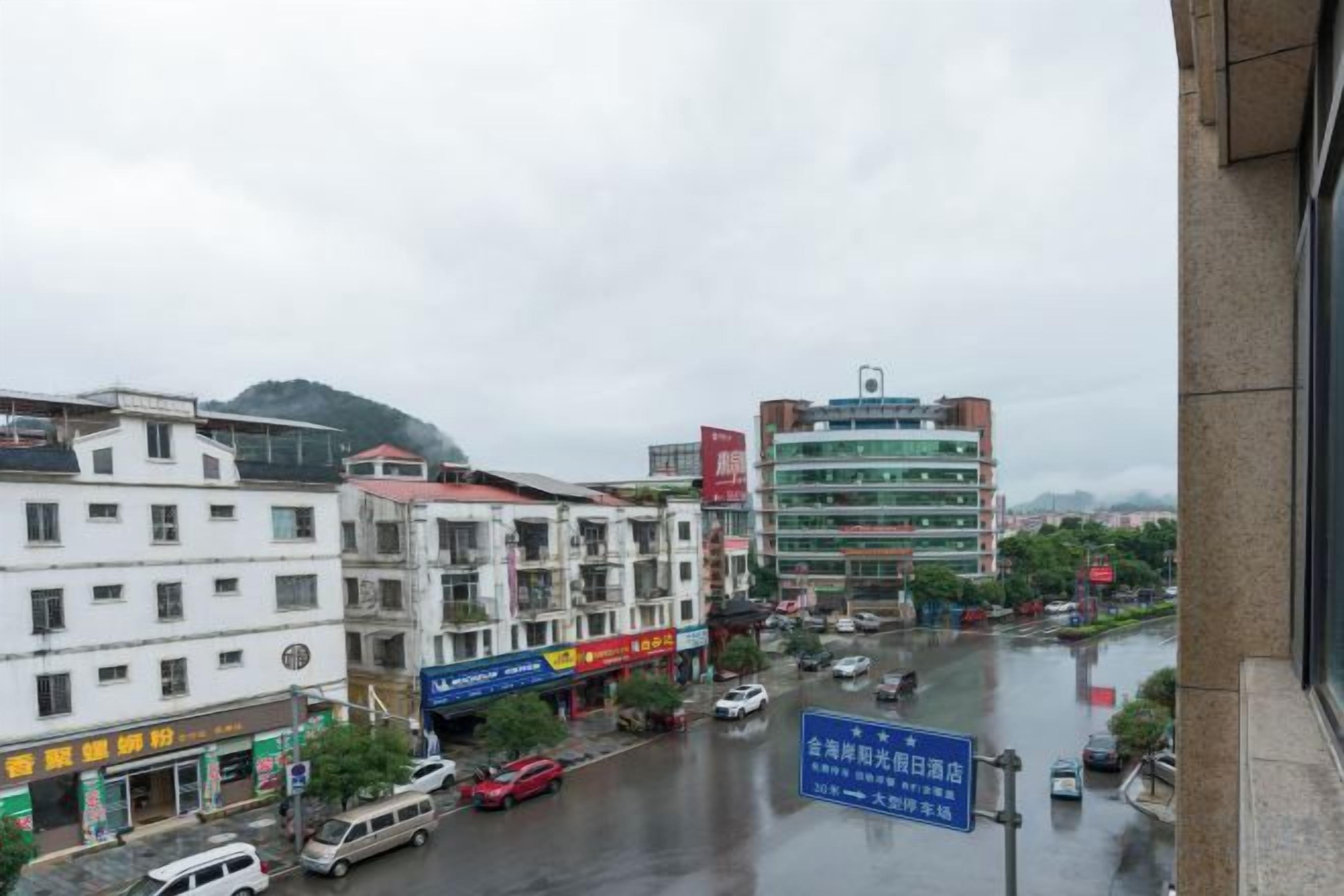 A multi-story building with a commercial ground floor, a parking lot, and a view of a wet street with cars.