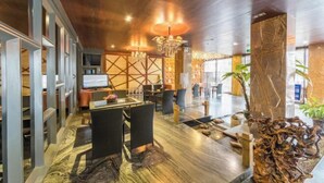 Un moderno vestíbulo de hotel con techo de madera, una lámpara central de araña y una zona de estar con sillones de mimbre.