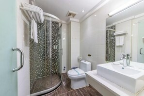 Un baño moderno con cabina de ducha de vidrio, inodoro blanco y un lavamanos grande de color blanco con espejo.
