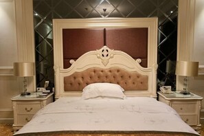Una cama grande con cabecera capitonada, dos mesitas de noche y un candelabro sobre ella.