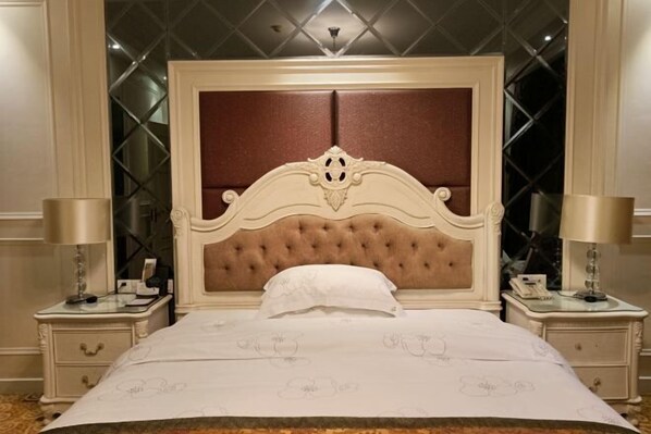 Una cama grande con cabecera capitonada, dos mesitas de noche y un candelabro sobre ella.