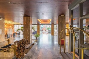 A hotel lobby with a marble floor, a reception desk, and a staircase.