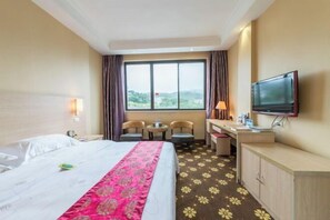 Habitación de hotel con cama, escritorio, silla, televisor y ventana con vistas al exterior.