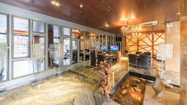 Un vestíbulo de hotel moderno con piso de mármol, una fuente central y una pantalla de televisión.