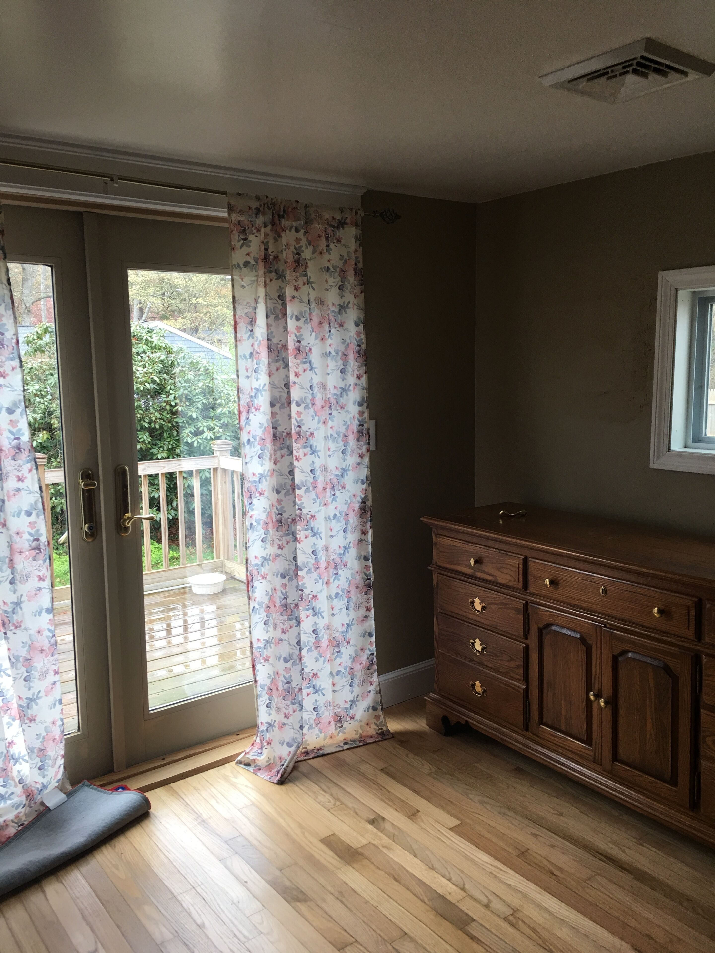 Een kamer met een schuifdeur naar een houten terras, een houten dressoir met lades, en een raam in de muur.