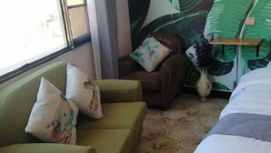 A hotel room with a green sofa, a bed, a chair, and a wall with a tropical leaf pattern. - Nianlun Theme Hotel (Ninglang)