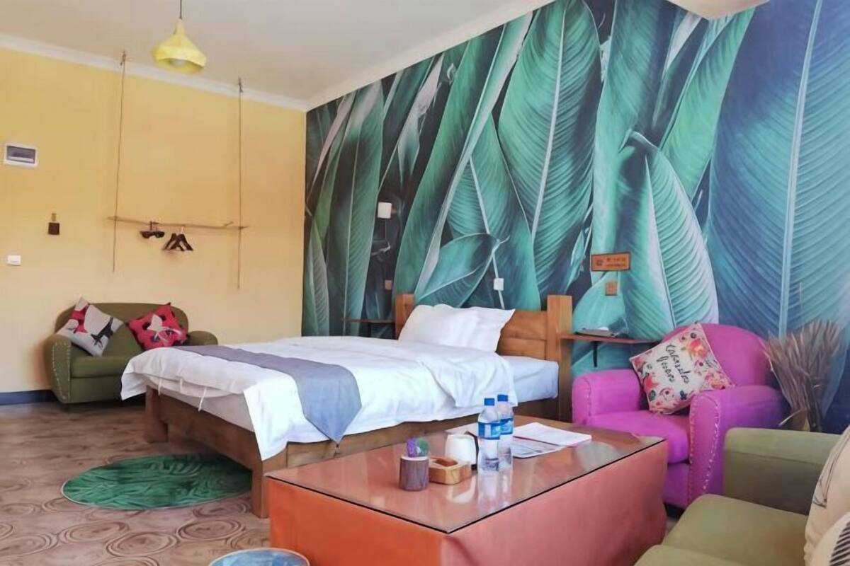 Una habitación con una cama, un sofá, una mesa de centro y una pared con un diseño de hojas.