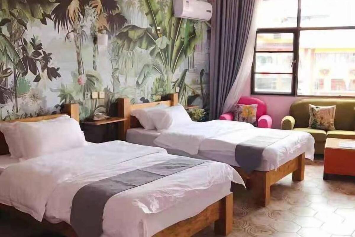 Una habitación con dos camas, un sofá, una ventana con cortinas y un mural tropical en la pared.