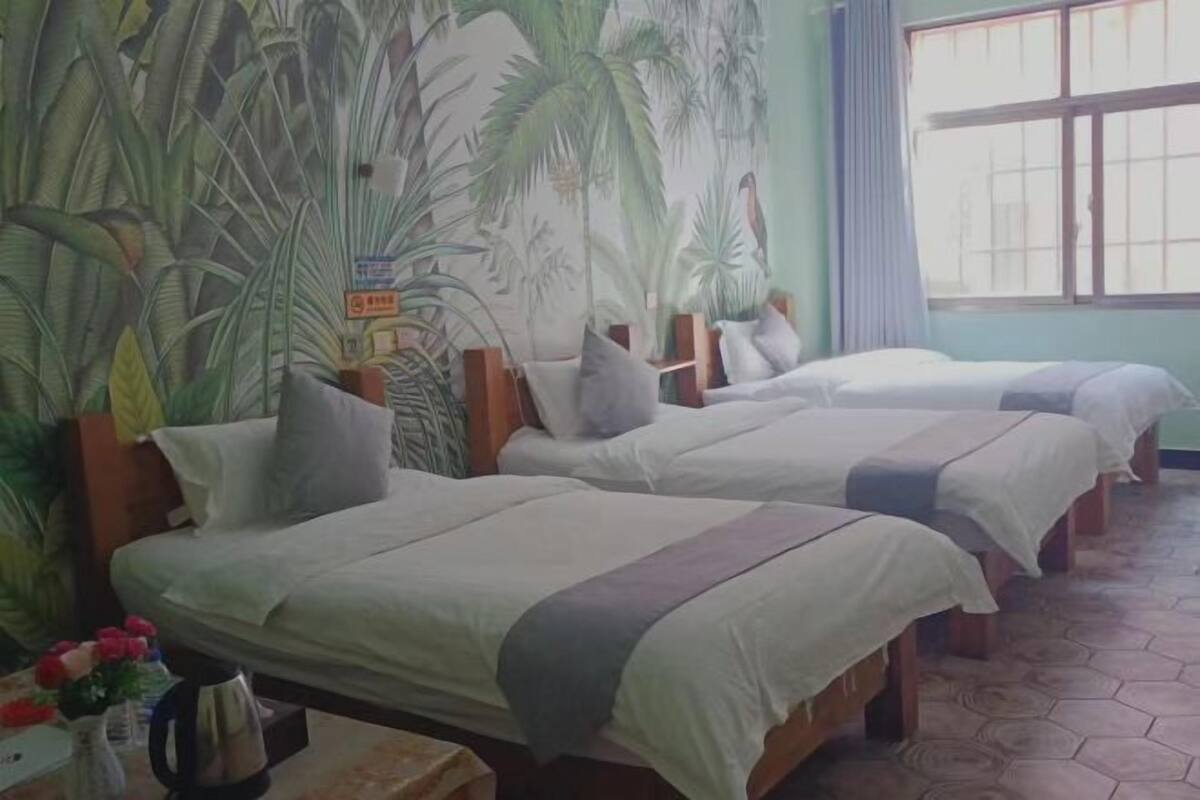 Habitación con tres camas, un ventanal grande y un mural de plantas tropicales en la pared.