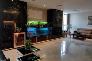 A lobby with a reception desk, a fish tank, a sofa, and a coffee table. - Yusheng Hotel (Qiannan)