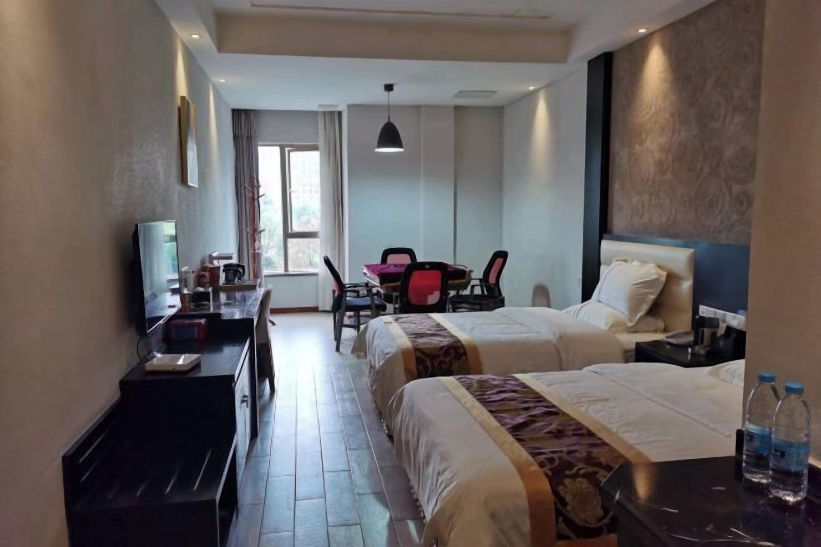 A hotel room with two beds, a desk with a chair, a TV, and a window.