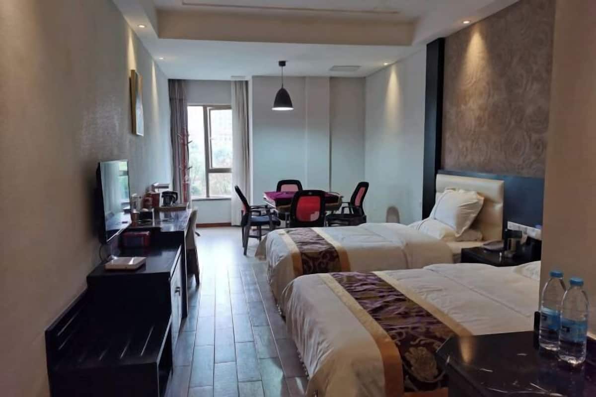 Une chambre d’hôtel avec deux lits, un bureau avec une chaise, une télévision et une fenêtre.