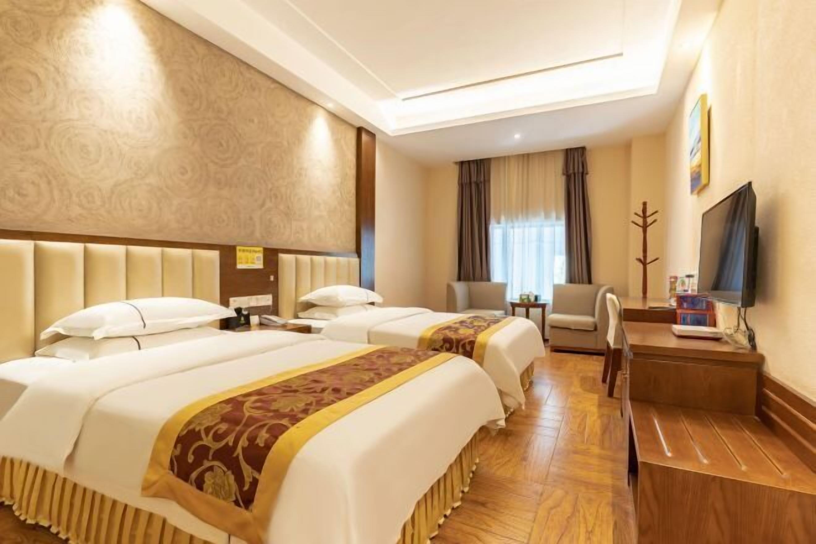 A hotel room with two beds, a desk, a chair, a television, and a window with curtains.