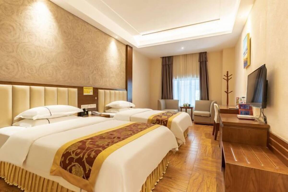 Une chambre d’hôtel avec deux lits, un bureau, une chaise, une télévision et une fenêtre avec des rideaux.