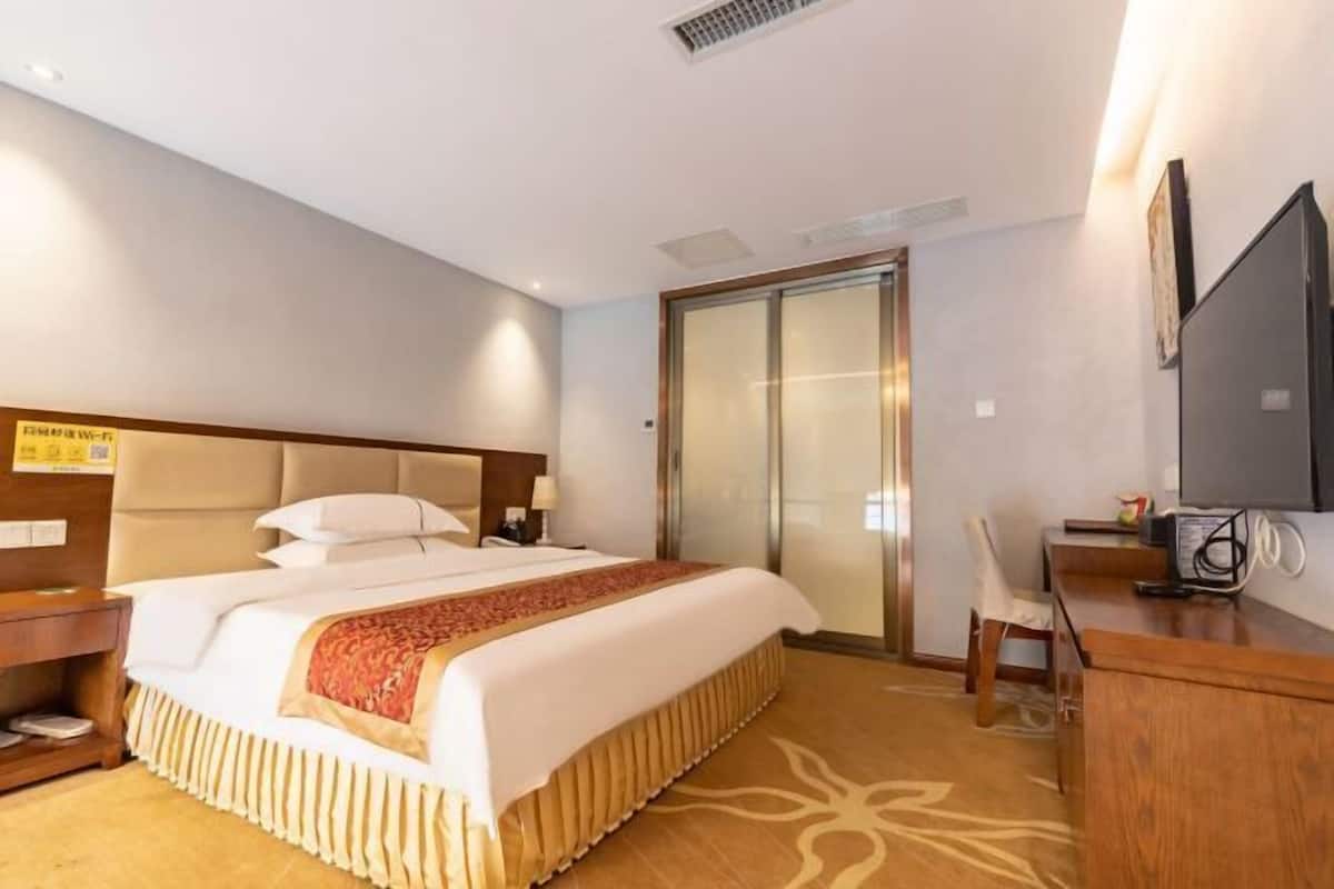 Une chambre d’hôtel avec un grand lit, un bureau, une chaise, une télévision et une porte coulissante.
