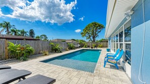 A rectangular swimming pool with a tiled deck, surrounded by a wooden fence and various plants. There are blue chairs and a table on the deck. - 19th - Aunies Place · Totally Updated Pool/FUN/Beaches (Bradenton)