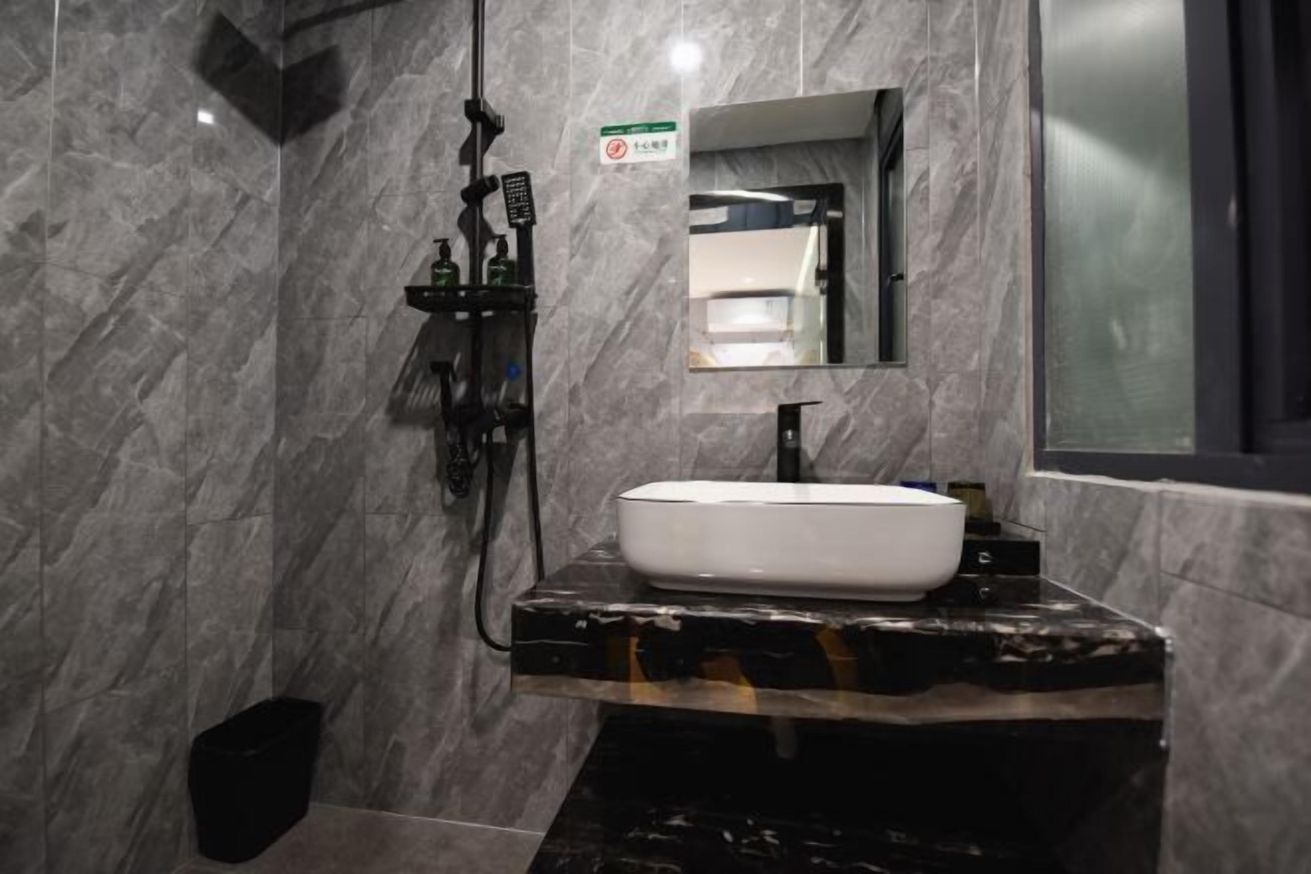 Un baño con pared de mármol, un lavamanos blanco, un espejo y zona de ducha.