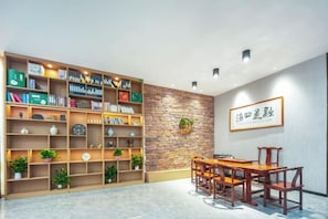 A room with a wooden bookshelf, a dining table with chairs, and a stone wall with a framed sign. - Zhicheng Select Hotel (Yongzhou Vocational and Technical School) (Yongzhou)