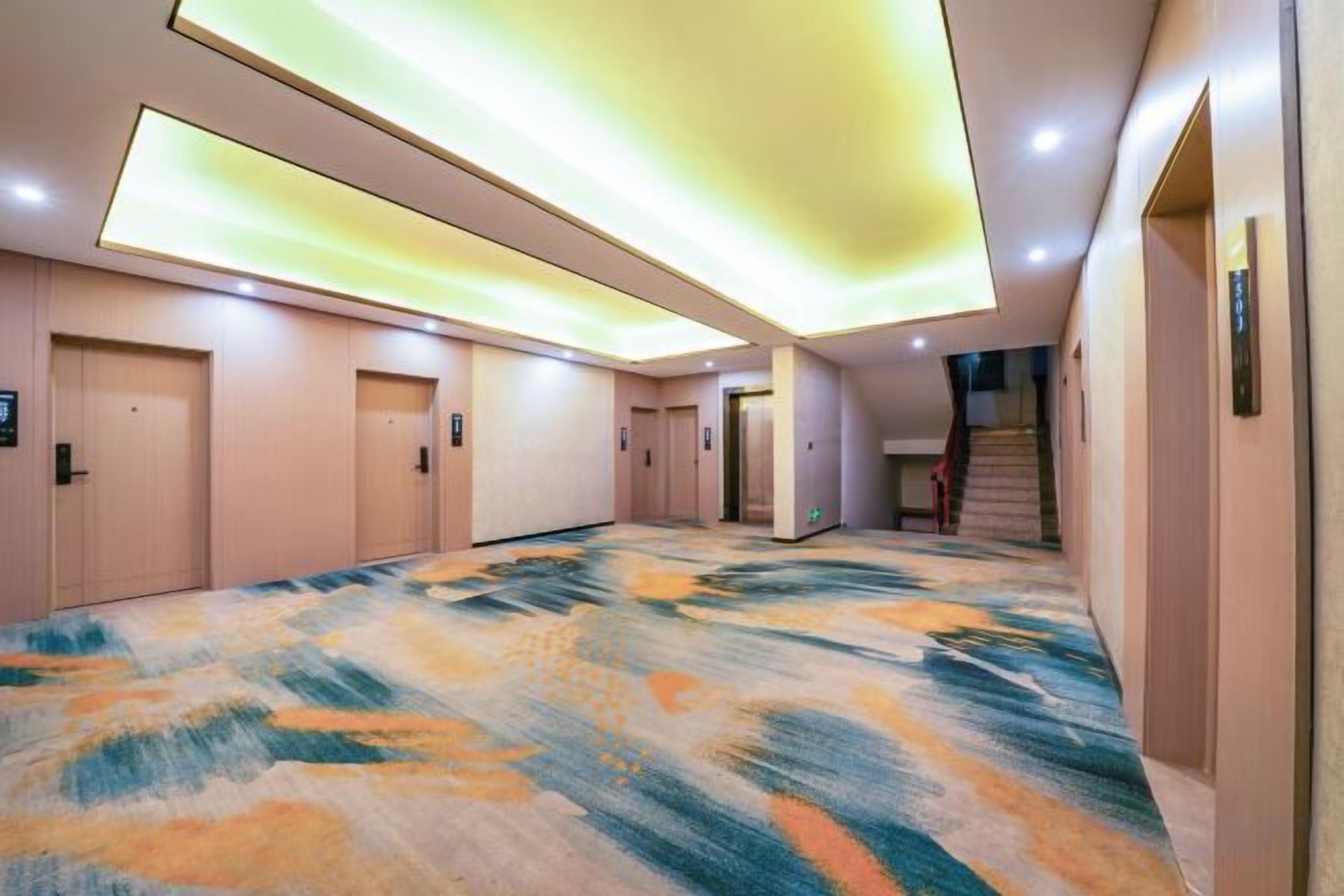 A hotel hallway with carpeted flooring, doors, and a staircase.