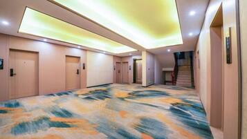 A hotel hallway with carpeted flooring, doors, and a staircase.
