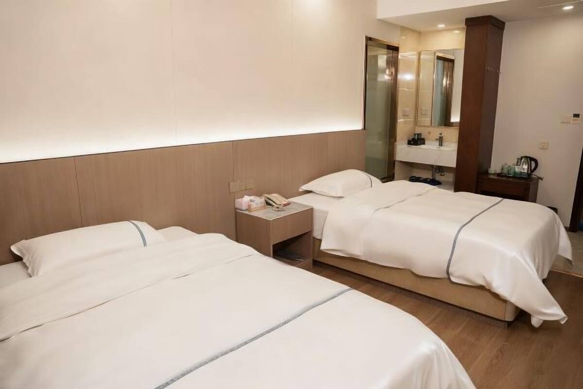 A hotel room with two beds, a nightstand, a mirror, and a wooden floor.