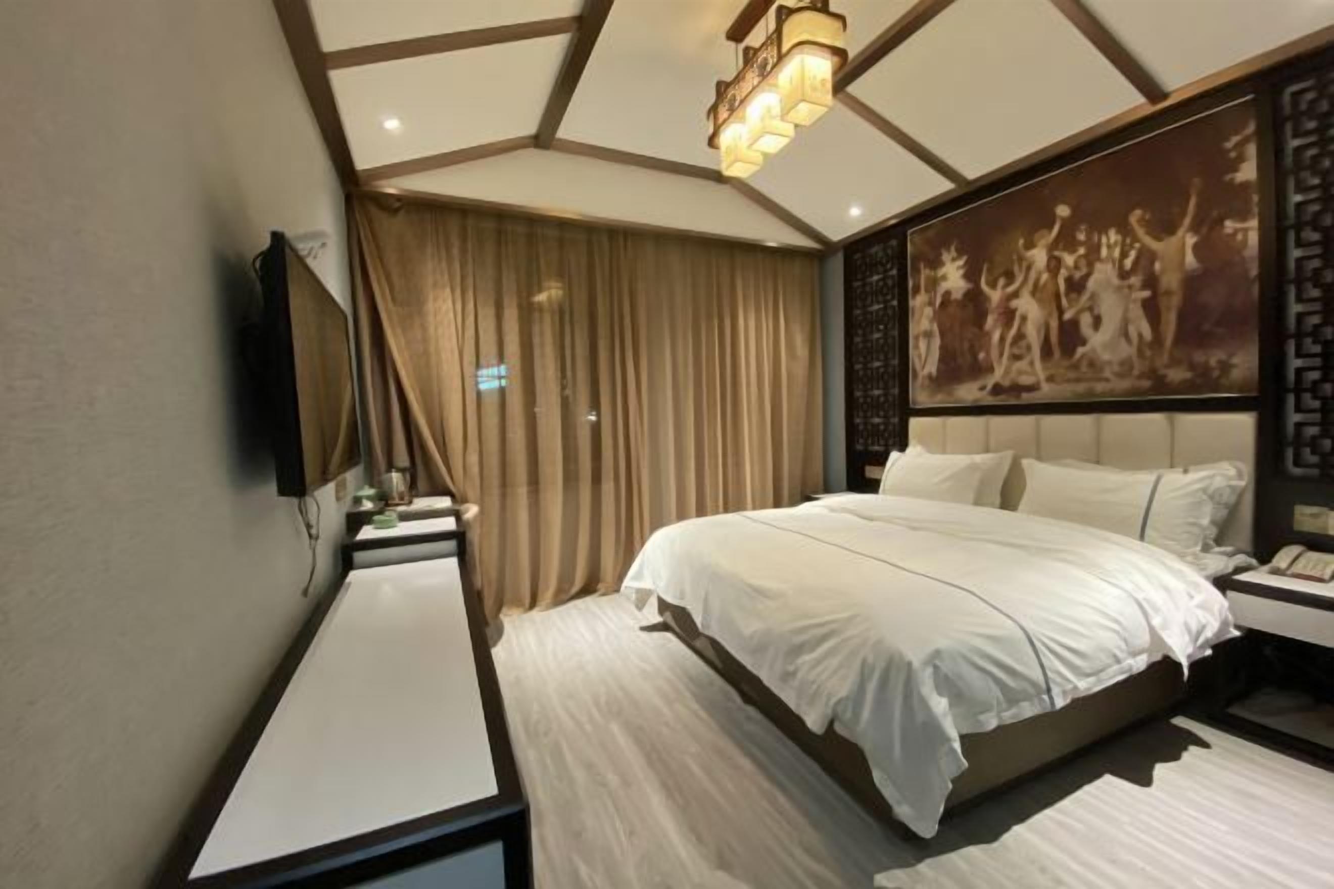 Una habitación de hotel moderna con una cama grande, un televisor de pantalla plana montado en la pared, una mesita de noche y un cuadro decorativo.