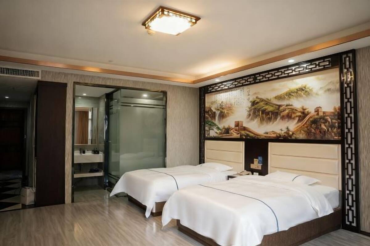 A hotel room with two beds, a large painting on the wall, and a modern bathroom.