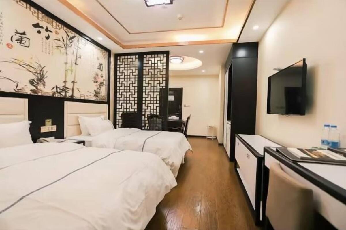 A hotel room with two beds, a desk, a TV, and a decorative screen with calligraphy.