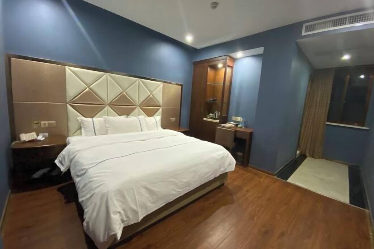 A hotel room with a large bed, a nightstand, a dresser, a mirror, and a window.