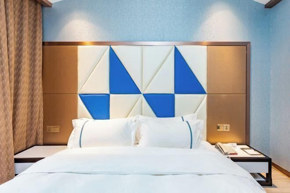 A hotel room with a bed, a nightstand, a wall with geometric patterns, and a curtain.
