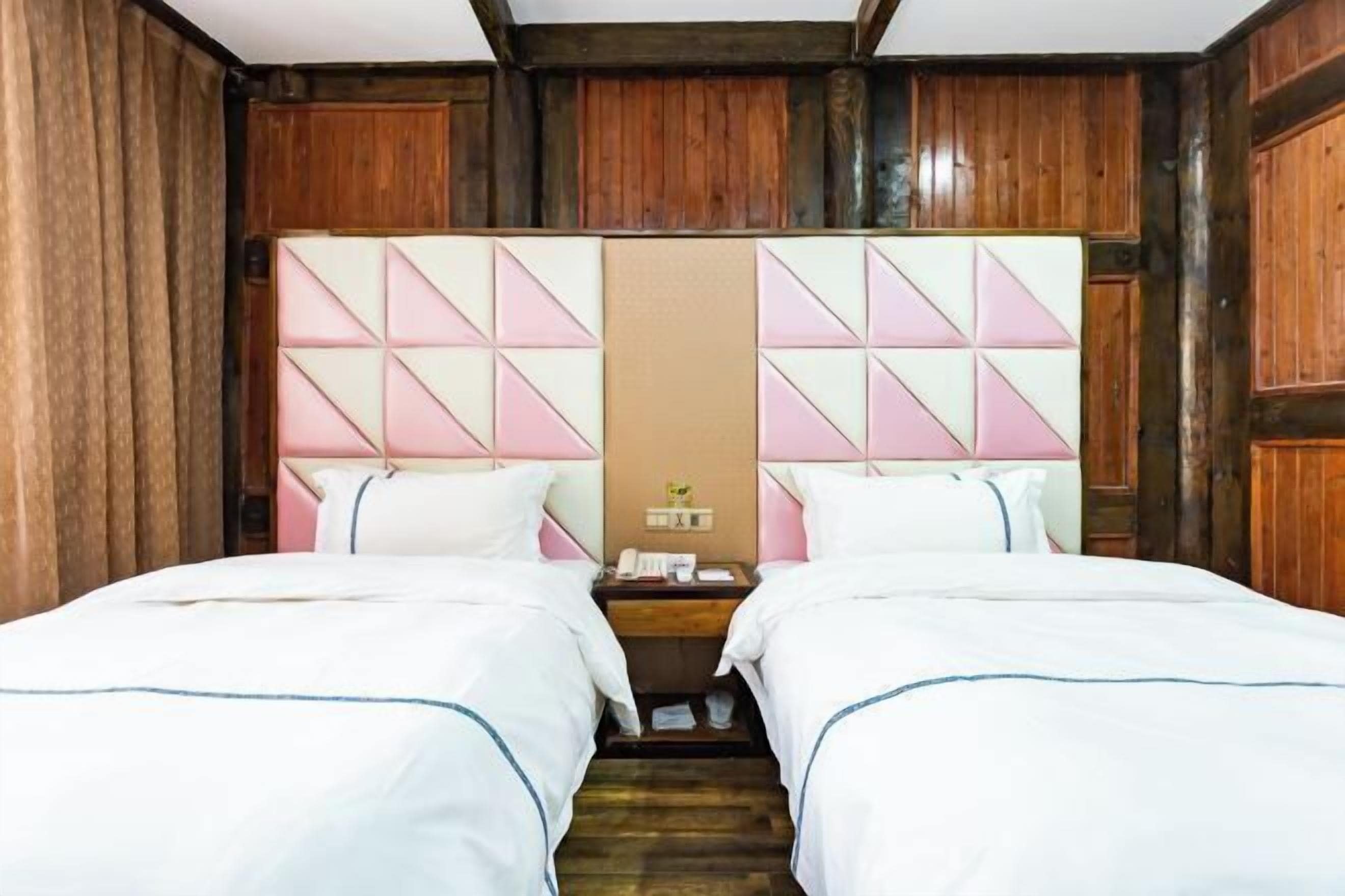 A double room with two beds, wooden paneling, a nightstand with a phone, and a mirror on the headboard.