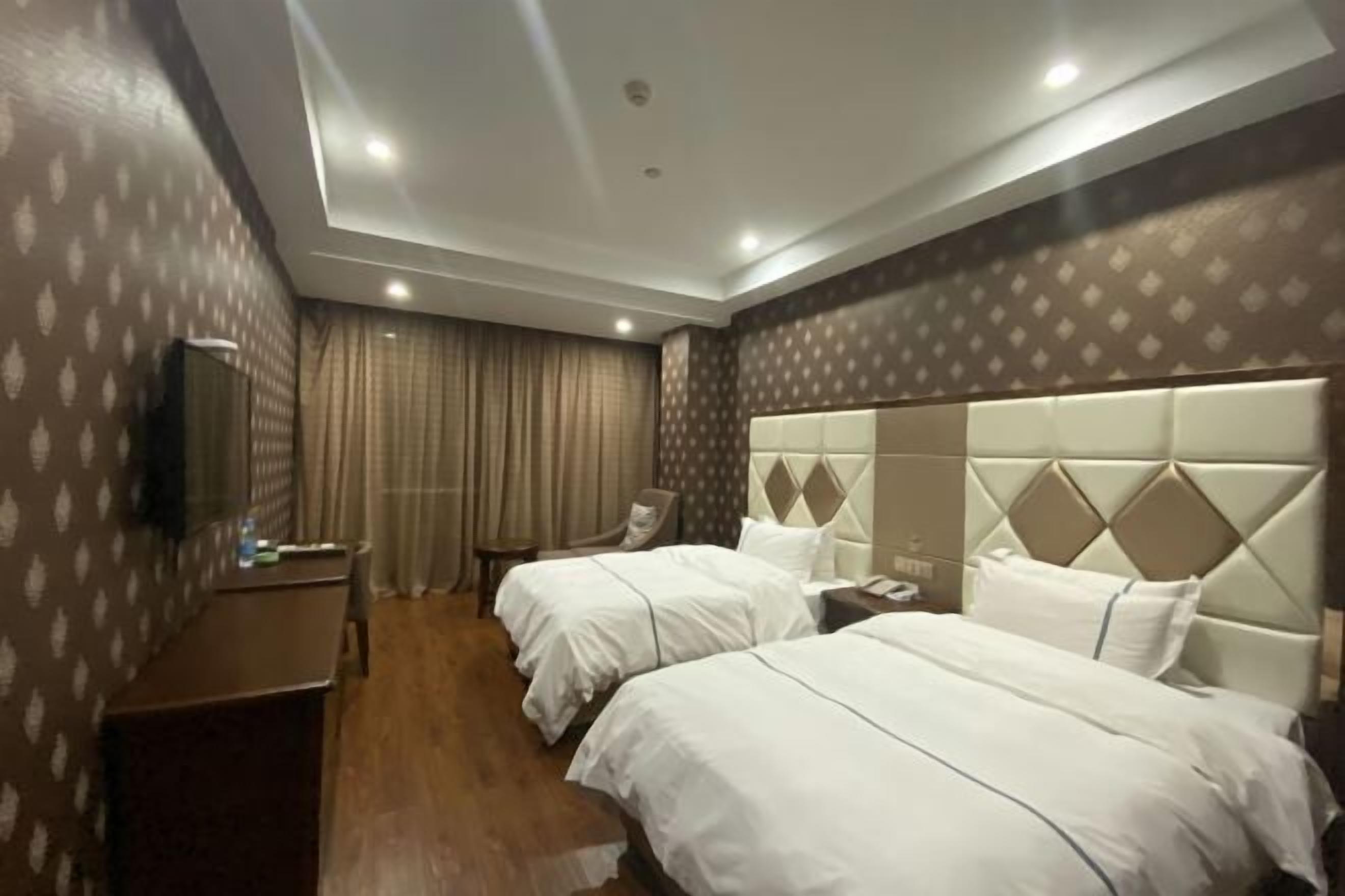 A hotel room with two beds, a desk, a chair, and a television.