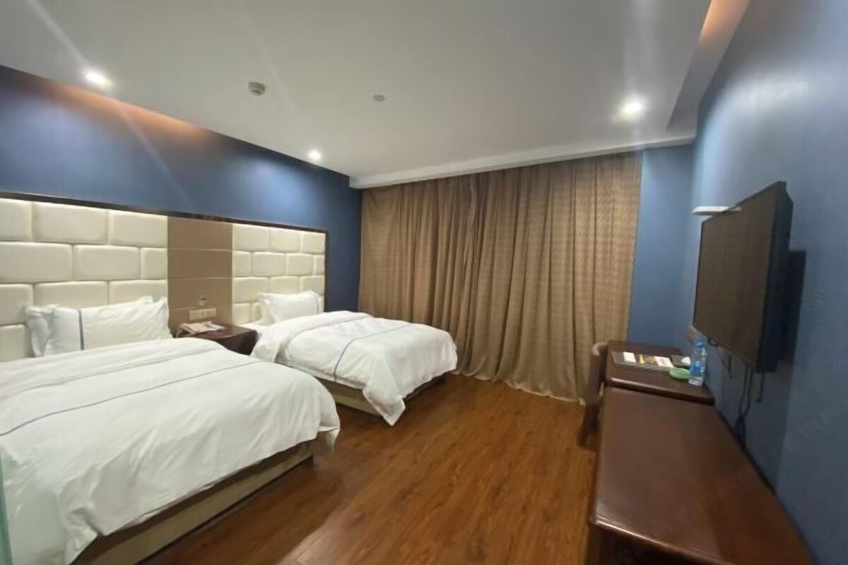 A hotel room with two beds, a wooden floor, a large headboard, a flat-screen TV, and a desk with a chair.