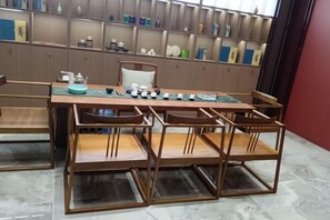 A dining area with a wooden table and chairs, a tea set, and shelves with decorative items. - Zijin Haoting Hotel (Renhuai)