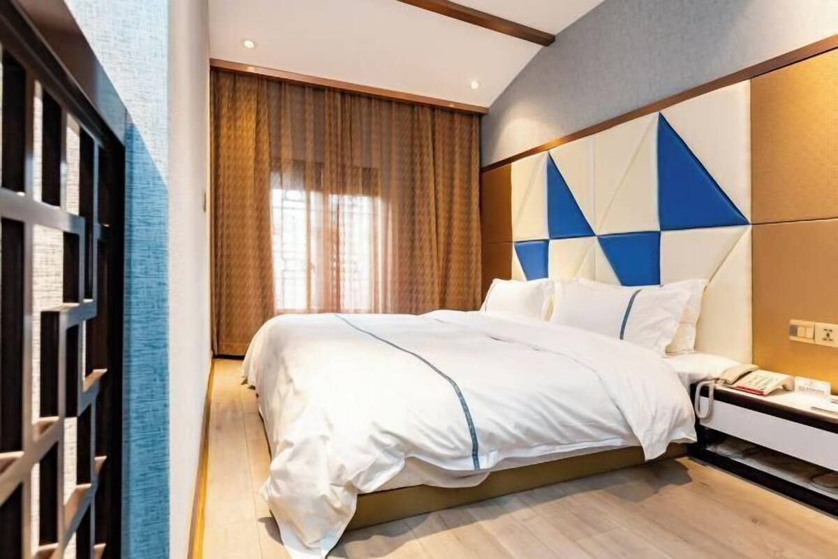 A modern hotel room with a large bed, a bedside table, and a view of a cityscape through the window.