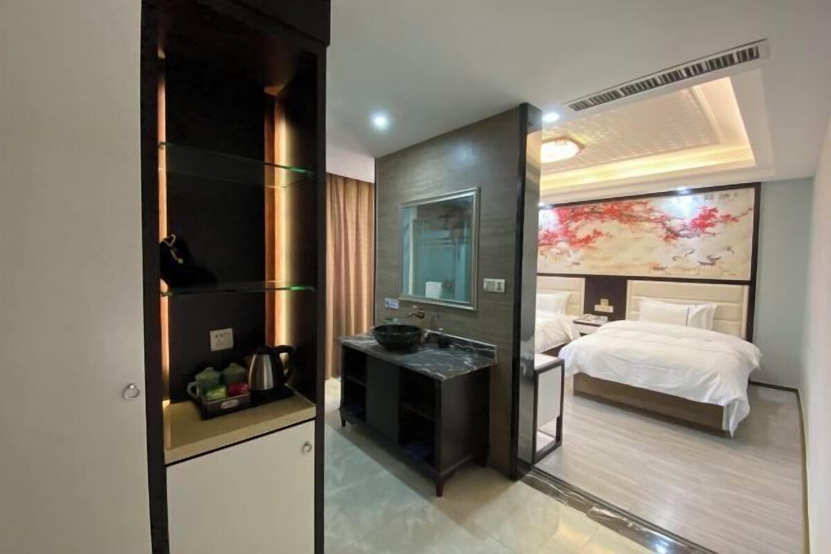 A hotel room with a bed, a bathroom with a sink and mirror, and a decorative wall piece.