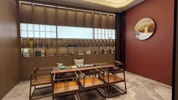 A room with a long table, chairs, a wall-mounted display case, and a round painting.
